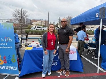 Two people standing in front of an informational booth at an outdoor event.