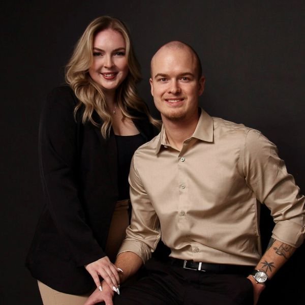 Smiling couple posing against a dark backdrop in stylish attire.