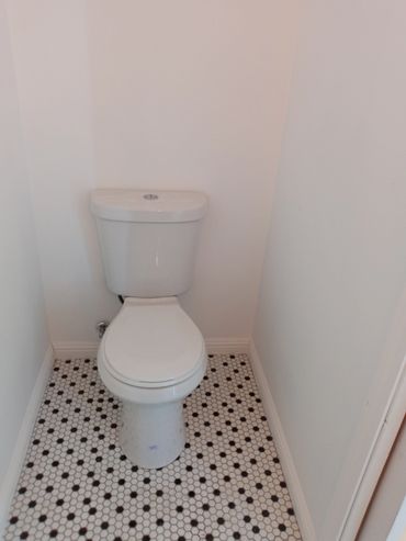 White toilet in a small bathroom with patterned tile floor.