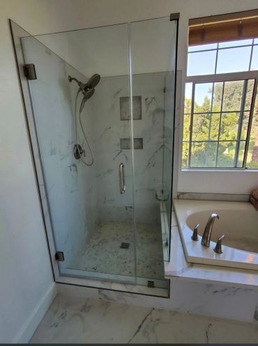 Modern bathroom with glass shower and bathtub beside a window.