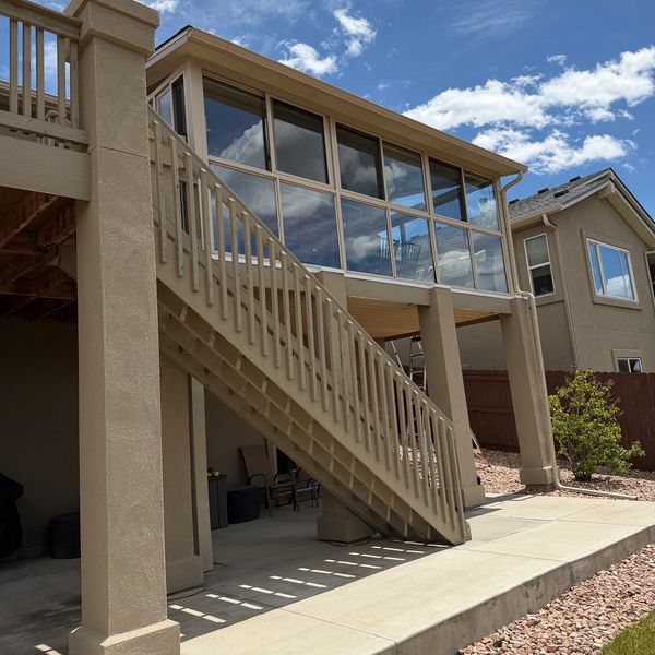 Outdoor staircase leading to a glass-enclosed balcony on a beige house under a partly cloudy sky.