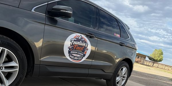 Gray car with a round business logo on the door under a cloudy sky.