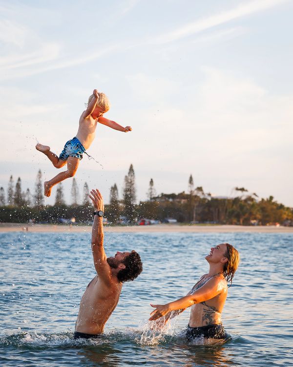 A man throws a child in the air while a woman watches joyfully in the water.