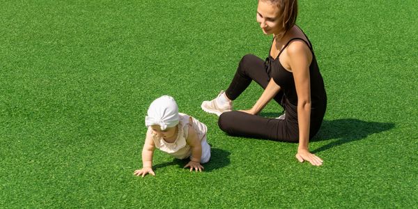 A woman watches a baby crawling on vibrant green grass.
