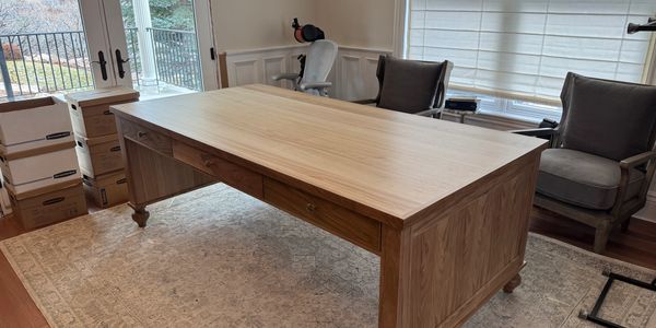 Large wooden desk in a room with chairs and boxes.