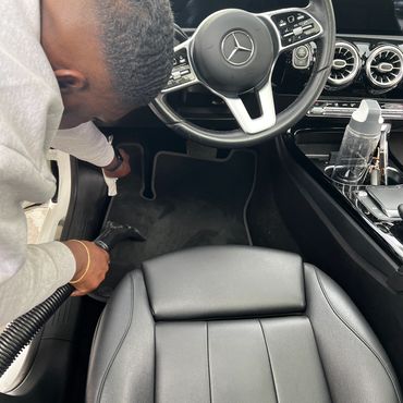Man vacuuming the floor mat inside a Mercedes car.