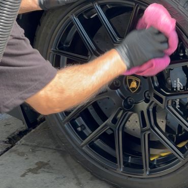 Person cleaning a Lamborghini car wheel with a pink cloth and black gloves.