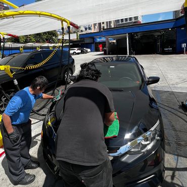 Two people washing and polishing a black car at a car wash station.