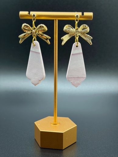 Gold bow earrings with pale pink geometric pendants on a gold stand.