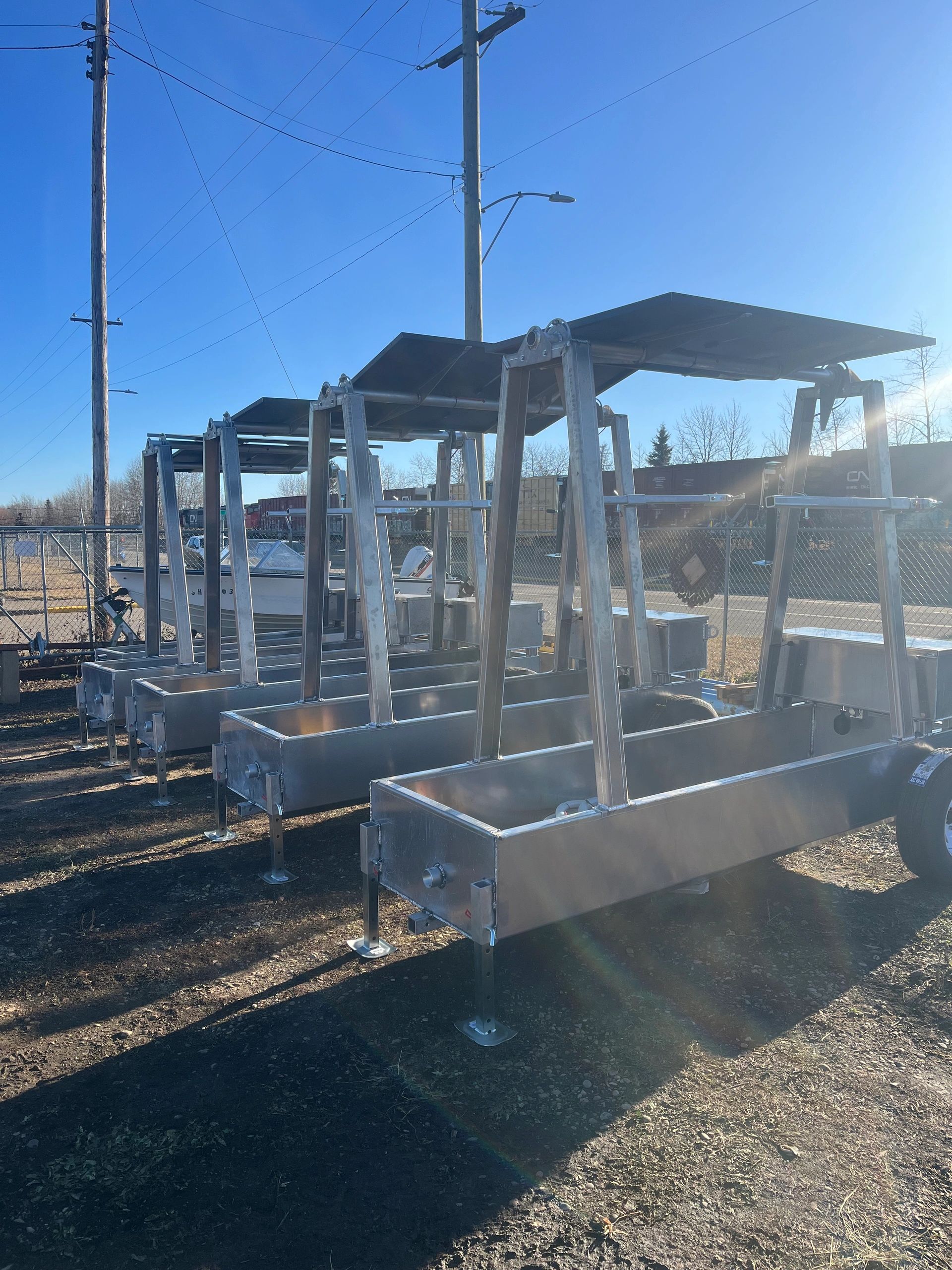 Multiple metal structures with overhead shades lined up outdoors on a sunny day.