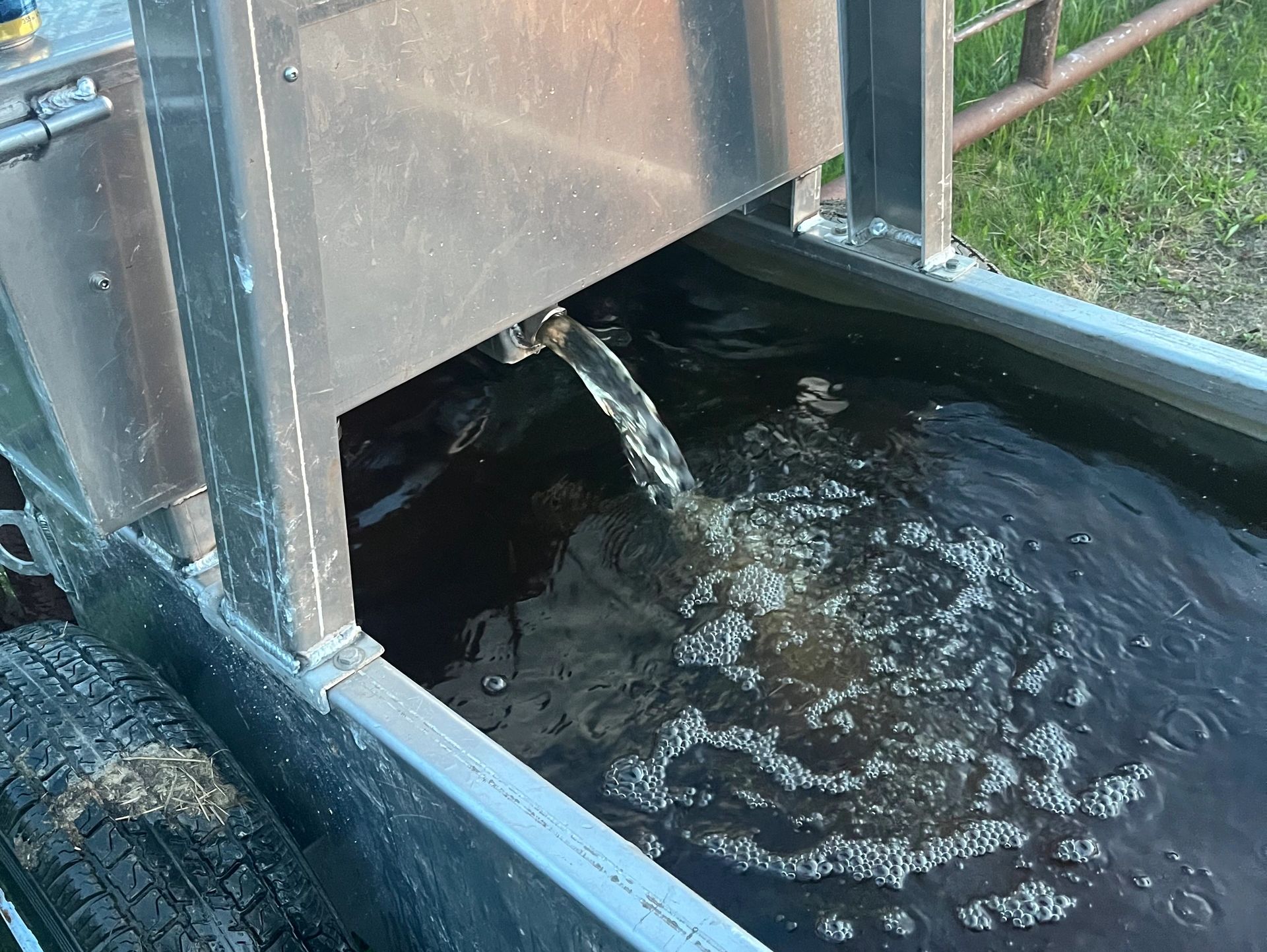 Water flowing from a metal spout into a container outdoors.