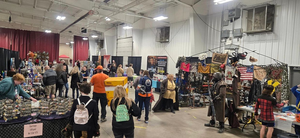 Indoor vendor market with people browsing various stalls and cosplay costumes.