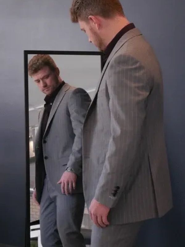 Man in a gray pinstripe suit looking at himself in a mirror.