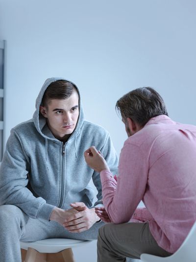 A young man in a grey hoodie listens intently to a therapist during a counseling session.