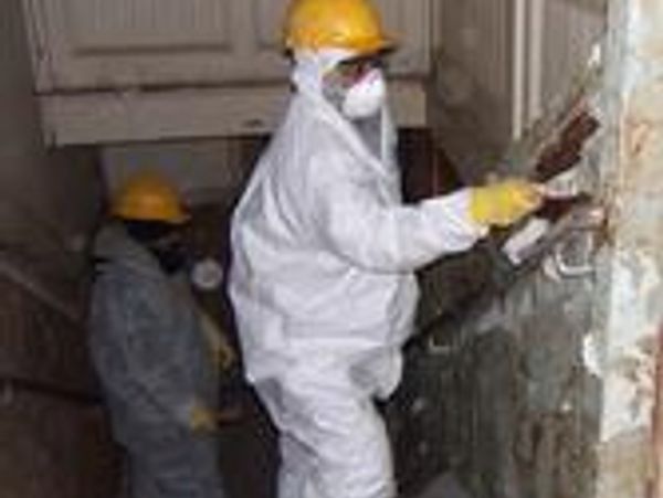 Workers in protective suits and helmets performing demolition work indoors.