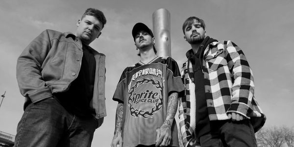 Three men pose confidently in casual streetwear, shot from a low angle in black and white.