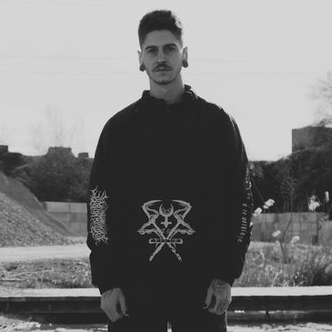 Man in dark hoodie with graphic design standing outdoors in black and white photo.