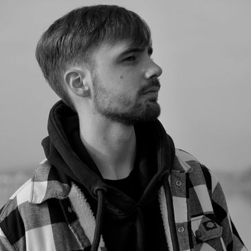 Young man in black hoodie and checkered jacket looking sideways.