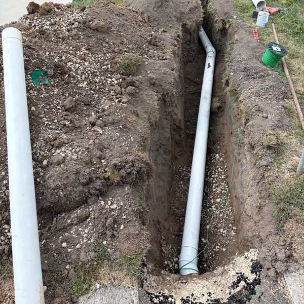 Trench with installed and uninstalled PVC pipes outdoors.