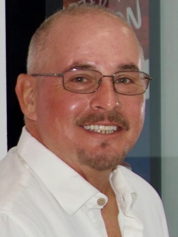 A middle-aged man with glasses smiling, wearing a white shirt.