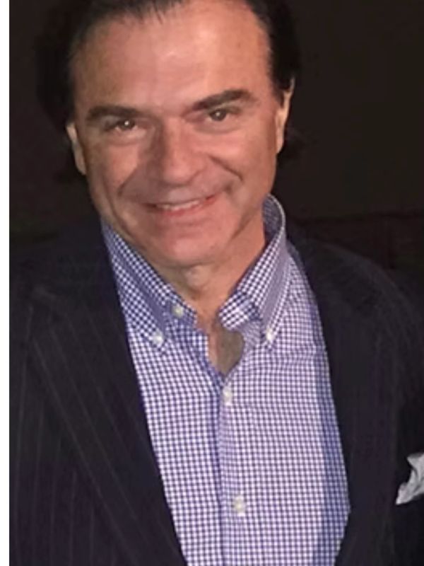 Smiling man wearing a checkered shirt and dark blazer.