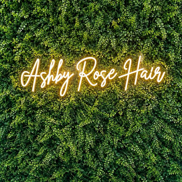 Neon sign reading 'Ashby Rose Hair' on green leafy wall.