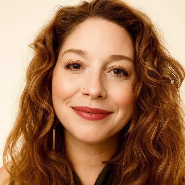 Smiling woman with long curly red hair and a nose ring.