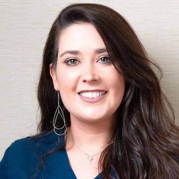 Smiling woman with long dark hair wearing teardrop earrings and a blue top.