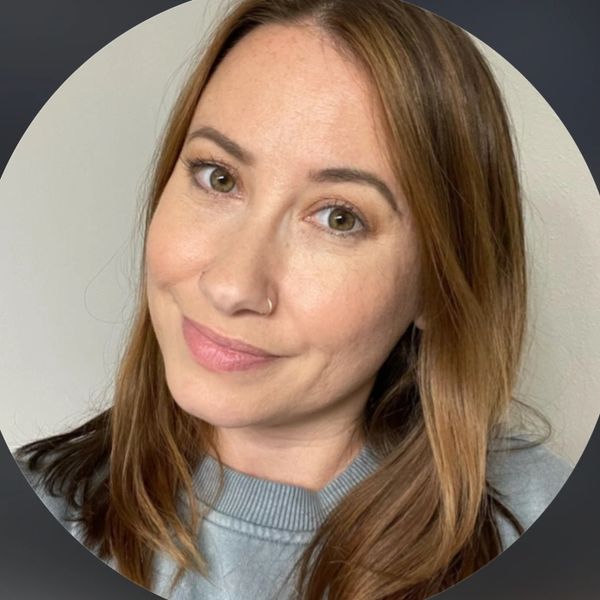 Smiling woman with light brown hair and a nose ring in a gray sweater.