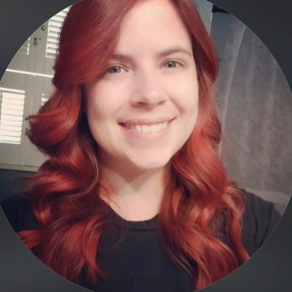 Smiling woman with long, wavy red hair and light eyes in a black top.