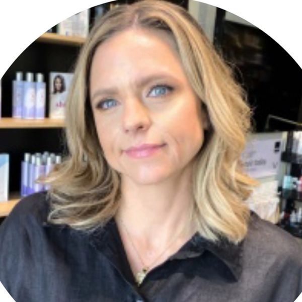 Blonde woman with blue eyes in a black shirt, smiling slightly indoors.