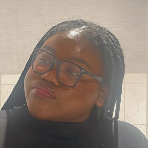 Woman with glasses and braided hair looking sideways.
