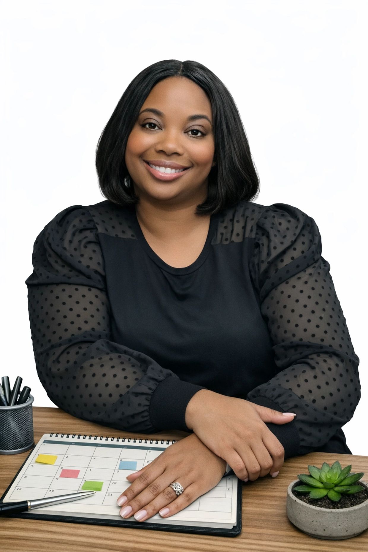 Smiling woman in black sitting at a desk with a planner and plant.