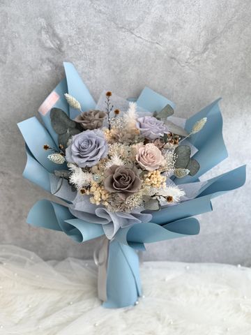 Elegant bouquet with muted pastel roses and dried flowers wrapped in blue paper.