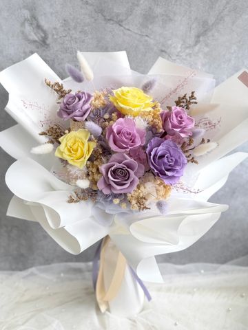 Elegant bouquet of yellow and purple roses wrapped in white paper.