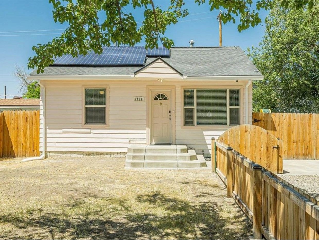 Small beige house with solar panels and fenced yard.