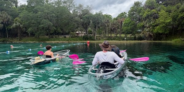 Two people kayaking on clear water with pink paddles.