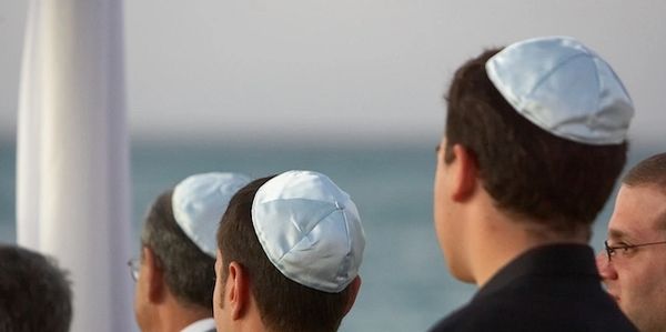 Men wearing white kippahs at a seaside gathering.
