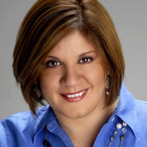 Smiling woman with short brown hair wearing a blue shirt and jewelry.