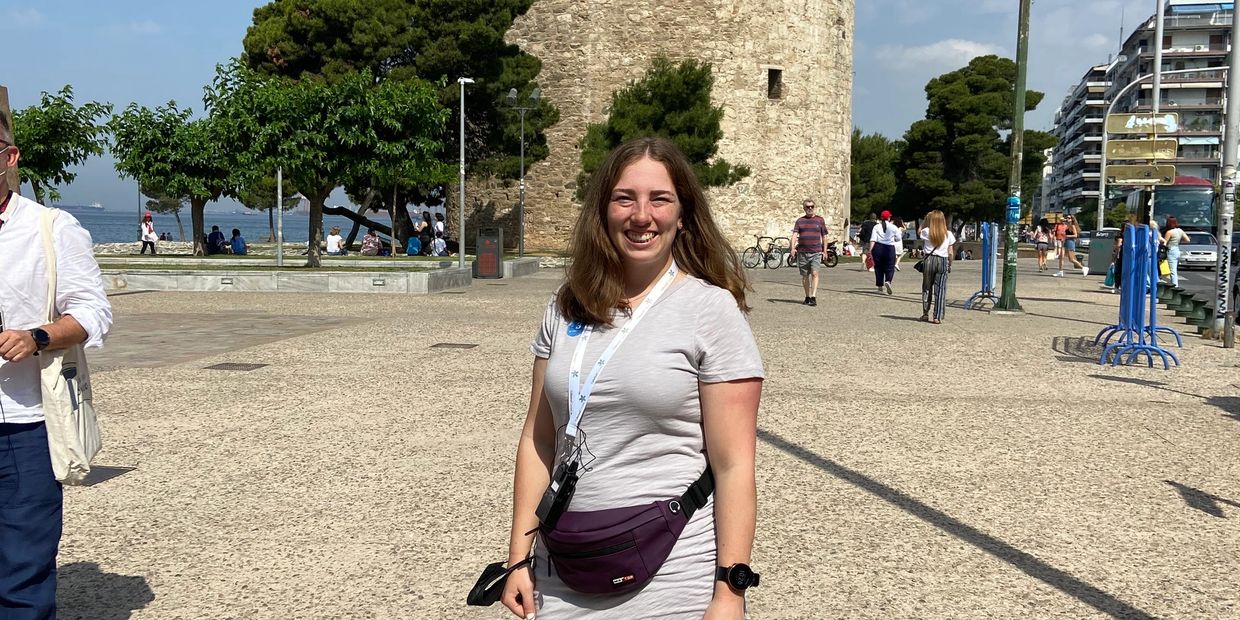 A smiling woman stands in front of the historic White Tower on a sunny day.
