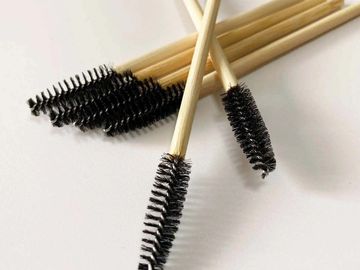 Close-up of several disposable mascara wands with wooden handles on a white surface.