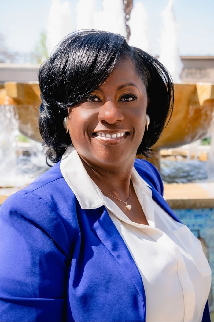 Confident woman in blue blazer smiling by a fountain.