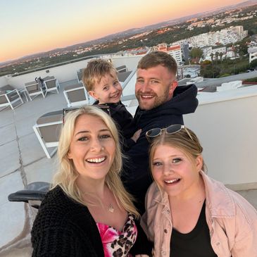 Smiling family enjoying a rooftop sunset with city views.