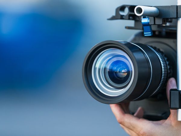 Camera lens attached to a camera and hand focusing close up detailed with smooth blue background