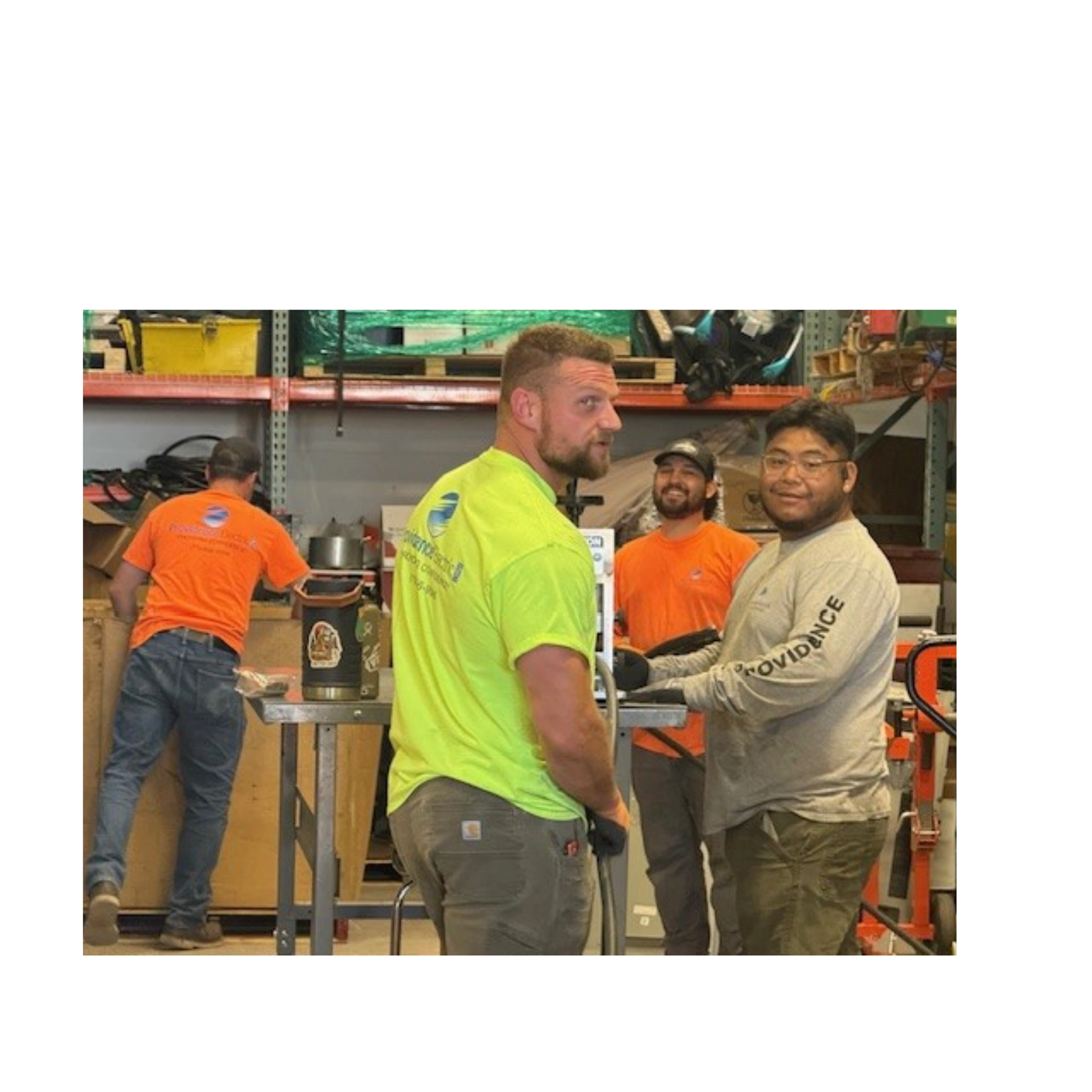 Four workers in a warehouse wearing bright shirts and engaged in tasks.