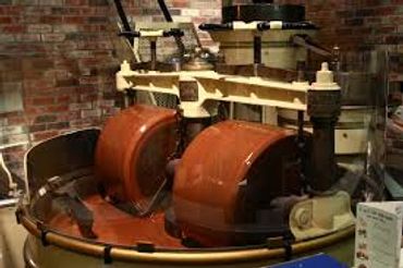 Vintage industrial machine with large rotating wheels and a brick background.