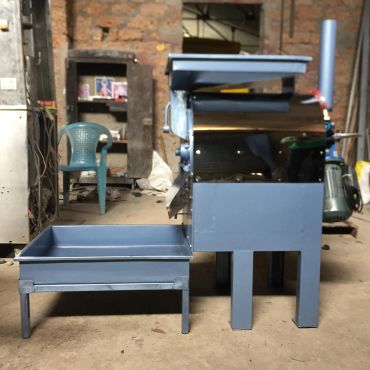 Metal machine with hopper and tray in a workshop setting.