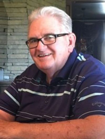 Smiling elderly man wearing glasses and a striped polo shirt.