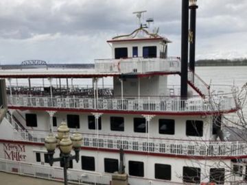 A large riverboat docked by the shore on a cloudy day.