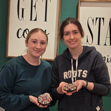 Two women holding decorated cookies and smiling.
